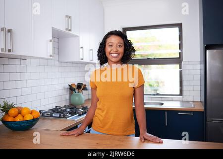 Eine junge, multiethnische Frau lächelt und steht in einer kleinen, sauberen Küche Stockfoto