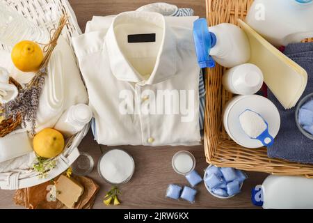 Detailvergleich von ökologischen Wäschereireinigungsprodukten auf Holztisch und Chemikalien auf weißem Tisch. Draufsicht. Horizontale Zusammensetzung. Stockfoto