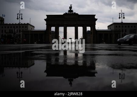 Berlin, Deutschland. 26. August 2022. Eine Person mit Sonnenschirm läuft vor dem Brandenburger Tor. Quelle: Christoph Soeder/dpa/Alamy Live News Stockfoto