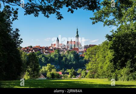 Schöner Blick auf die malerische Altstadt von Tabor, eingerahmt von grünen Ästen am blauen Himmel. Blick auf die gotische Kirche im historischen Zentrum der mittelalterlichen hussitischen Stadt. Stockfoto