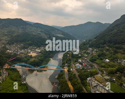 Luftaufnahme der blauen Brücke über den Fluss in der Berglandschaft in der Dämmerung Stockfoto