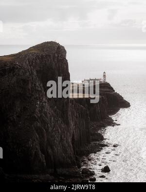 Die vertikale Ansicht eines Leuchtturms am Rand der Klippe am Meer unter dem wolkigen Himmel Stockfoto
