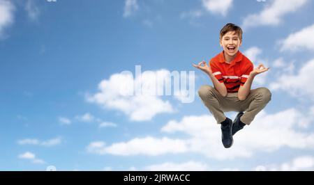 Glücklicher Junge, der in Yoga-Pose über dem Himmel fliegt Stockfoto