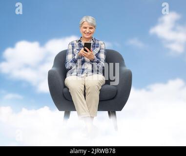 Lächelnde ältere Frau mit Smartphone im Stuhl Stockfoto