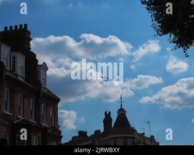 Flugzeug fliegt über Dächer mit Wolken am Himmel Stockfoto