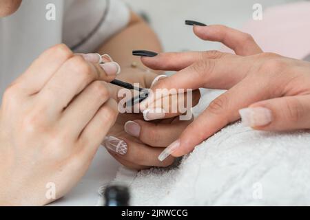 Detail der Hände eines Manikuristen Malerei die Nägel mit einem schwarzen Nagellack. Gestaltung und Verschönerung der Nägel einer Frau, die in der Schönheit s ist Stockfoto