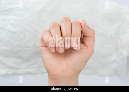 Hand einer Latina-Frau, die ihre Nägel in einer geschlossenen Handpose zeigt, im Hintergrund ein weißes Handtuch, halb angeordnete Nägel, die für Nagellack und Dekor bereit sind Stockfoto