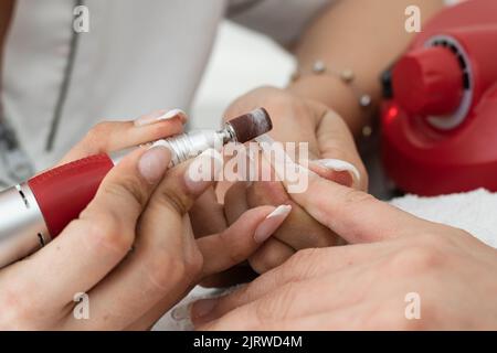 Detail der Hand des Latina-Manikuristen, Schleifen des Polygel-Nagels mit einem elektrischen Nagelpuffer, Entfernen von Unvollkommenheiten und lassen es perfekt und fertig Stockfoto