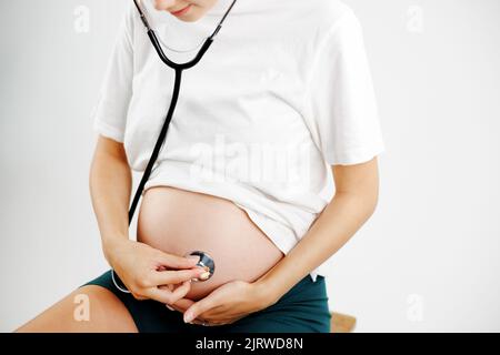 Schwanger Frau mit Stethoskop auf Bauch aufmerksam auf das Baby hören.. Stockfoto