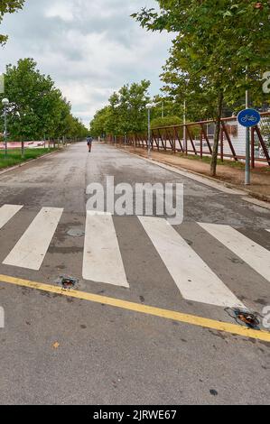 Crosswalk im Vordergrund mit einer Person auf einem Roller im Hintergrund. Stockfoto