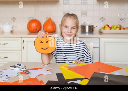 Lächelndes Mädchen, das Kunsthandwerk und Dekorationen für Halloween macht. Stockfoto