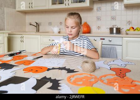 Ein Mädchen schneidet Papierbasteln für Halloween mit einer Schere aus. Stockfoto