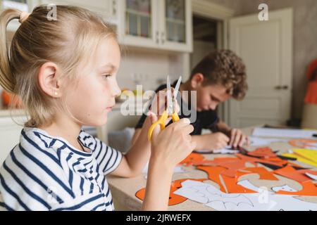 Bruder und Schwester basteln aus farbigem Papier für Halloween. Stockfoto