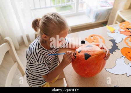 Ein Mädchen malt einen Kürbis mit Farben für Halloween. Stockfoto