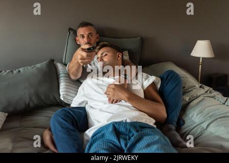 Homosexuell männlich paar im Bett. Einer schaut fern, während der andere schläft Stockfoto