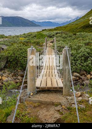 Kleine Hängebrücke über einen kleinen Bach auf einem Pfad entlang des Ufers des Bygdin-Sees im Jotunheimen-Nationalpark Norwegen Stockfoto