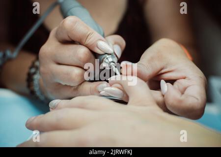 Manikuristen Hände machen Maniküre mit professionellen elektrischen Nagelfeile Drill, Maniküre-Tool im Schönheitssalon Stockfoto