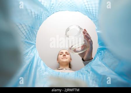 Frau wirft Glasglas in den Mülleimer Stockfoto