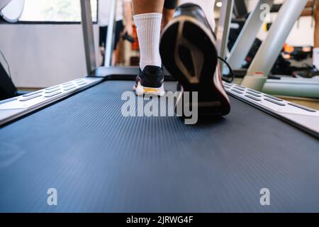 Boden des nicht erkennbaren männlichen Athleten in Turnschuhen, der tagsüber auf dem Laufband während des Cardio-Trainings in einem leichten Fitnessstudio läuft Stockfoto