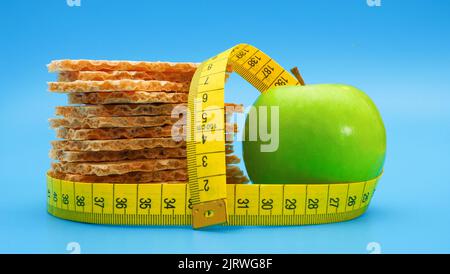 Stapel Roggenknusprig und grüner Apfel auf blauem Hintergrund, eingewickelt mit gelbem Maßband Stockfoto