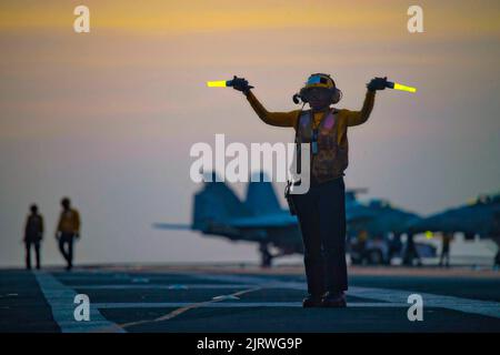 Palma, Spanien. 24. August 2022. U.S. Navy Aviation Boatswain Mate 3. Class Nadia Chapel leitet F/A-18F Super Hornet Kampfflugzeuge für den Nachtbetrieb auf dem Flugdeck des Nimitz-Klasse Flugzeugträgers USS Harry S. Truman, 24. August 2022 vor der Küste Mallorcas, Spanien. Kredit: MC3 Jack Hoppe/U.S. Navy/Alamy Live News Stockfoto