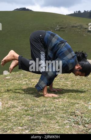 Ein junger Inder, der morgens im Berg die Bakasana Yoga-Pose (Krähenpose) praktiziert Stockfoto
