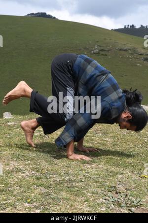 Ein junger Inder, der morgens im Berg die Bakasana Yoga-Pose (Krähenpose) praktiziert Stockfoto