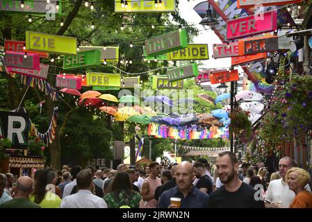 Manchester, Großbritannien. 26.. August 2022. Menschenmassen auf der Canal Street. Über der Straße hing ein Pronomen-Thema in kleinen Brettern. LGBTQ+ Pride, Manchester, Großbritannien, beginnt und geht über das Wochenende der Bankfeiertage vom 26.. Bis 29.. August in Manchesters Schwulendorf weiter. Die Organisatoren sagen: „Manchester Pride ist eine der führenden LGBTQ+-Wohltätigkeitsorganisationen Großbritanniens. Unsere Vision ist eine Welt, in der LGBTQ+-Menschen unbeschadet leben und lieben können. Wir sind Teil einer globalen Pride-Bewegung, die die Gleichberechtigung von LGBTQ+ feiert und Diskriminierung herausfordert.“ Quelle: Terry Waller/Alamy Live News Stockfoto