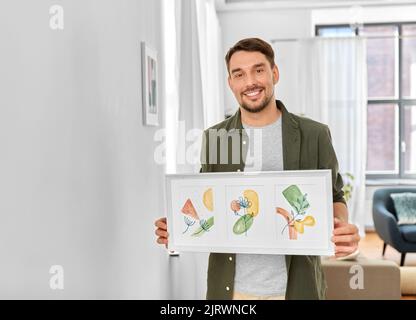 Lächelnder Mann, der das Haus mit einem Bild im Rahmen schmückt Stockfoto