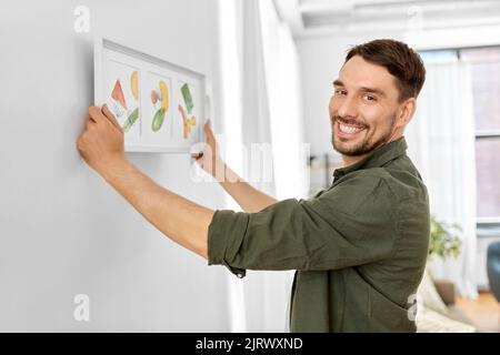 Lächelnder Mann, der das Haus mit einem Bild im Rahmen schmückt Stockfoto