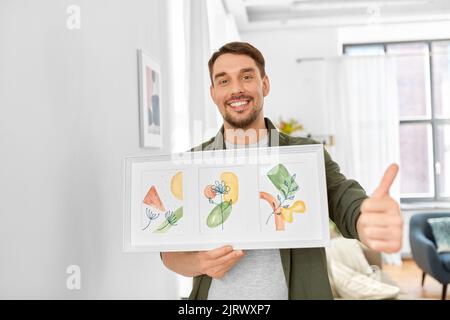 Lächelnder Mann, der das Haus mit einem Bild im Rahmen schmückt Stockfoto