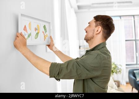 Lächelnder Mann, der das Haus mit einem Bild im Rahmen schmückt Stockfoto