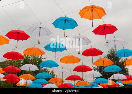 Bunte Regenschirme hängen beim Outdoor-Festival am bewölkten Himmel Stockfoto