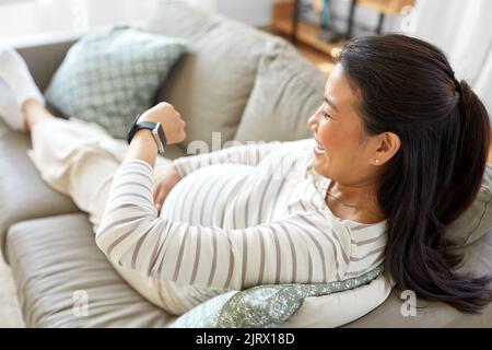 Glückliche Schwangere mit Smart Watch zu Hause Stockfoto