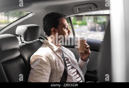 indischer Mann mit Kaffee zum Mitnehmen auf dem Rücksitz des Autos Stockfoto