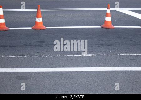 Eine Reihe orangefarbener Verkehrskegel auf einer grauen Autostraße. Stockfoto