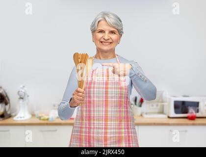 Lächelnde ältere Frau auf der Schürze mit Holzlöffeln Stockfoto