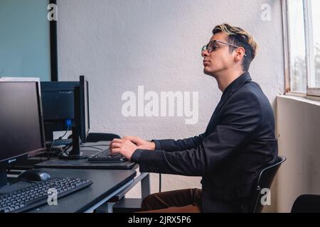 Ein Büroangestellter, der im Büro an seinem Computer arbeitet. Intelligenter Arbeiter am Schreibtischcomputer. Programmierer, der seine Arbeit mit vielen Computern macht. Hochwertige Fotos Stockfoto