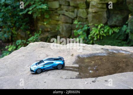 Das blaue Rennspielzeug-Modell von Blaufuppe in Metallic, in einer Naturszene, auf einem Felsen, der aus einer Wasserpfütze herausfährt. Stockfoto