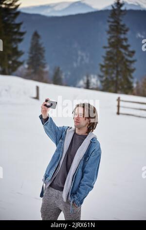 Selfi-Bergsteiger in verschneiten Bergen, mit Helm und Rucksack Stockfoto