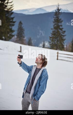 Selfi-Bergsteiger in verschneiten Bergen, mit Helm und Rucksack Stockfoto