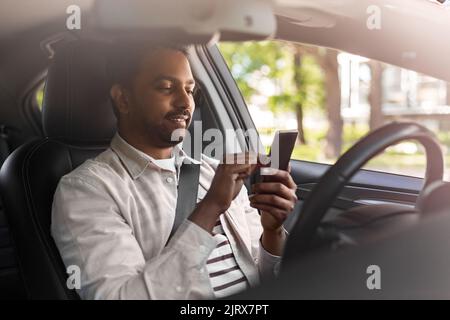 Lächelnder inder im Auto mit dem Smartphone Stockfoto