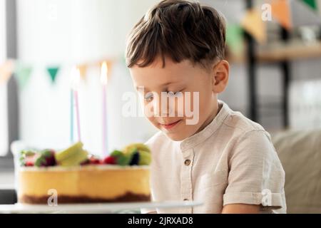 Glücklicher kleiner Junge, der Kerzen auf dem Geburtstagskuchen bläst Stockfoto