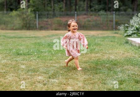 Glückliches kleines Mädchen, das barfuß auf Gras läuft Stockfoto