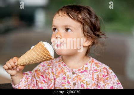 Glückliches kleines Mädchen, das Eis isst Stockfoto