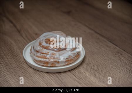 Schneckenbrötchen auf einem weißen Teller und Holzboden. Zimtrollen. Backwaren. Stockfoto