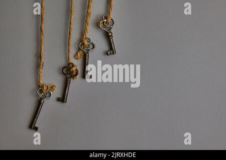 Nahaufnahme von vier dekorativen antiken Schlüsseln. Am braunen Seil hängen. Auf einem 50 präzenten grauen Hintergrund. Auf der linken Seite des Fotos. Stockfoto