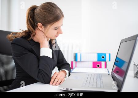 Junge Geschäftsfrau mit Nackenschmerzen im Büro Stockfoto