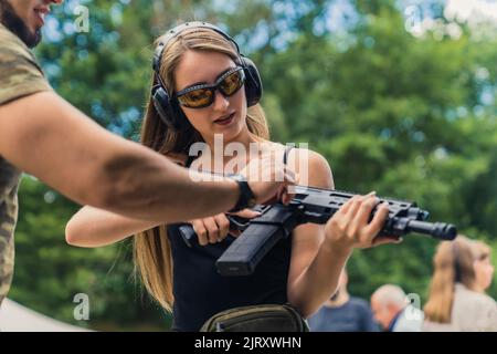 Ein hilfreicher Ausbilder erklärt seinem kaukasischen langgeharnten Kunden, der eine schützende Schießausrüstung trägt, wie man ein Gewehr verwendet. Mittlere Außenaufnahme. Hochwertige Fotos Stockfoto