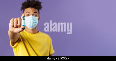 Medizin, Coronavirus und Menschen Konzept. Nahaufnahme des jungen Mannes in der Gesichtsmaske, die Ampulle mit dem Medikament hält, schließlich Impfstoff aus Kovid19 gefunden Stockfoto